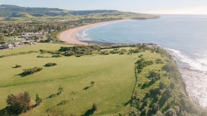 Drone photo of Gerringong, rolling hills and cliff face meet the ocean with houses. 